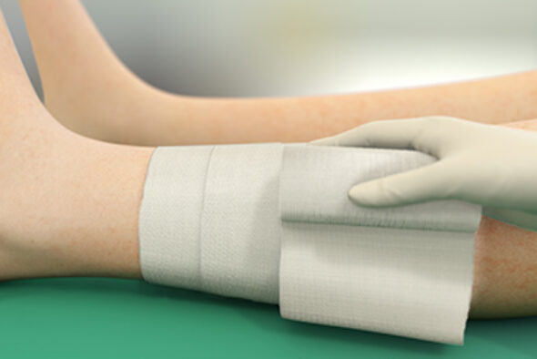 Person securing a Sorbact Absorption dressing with a fixation bandage around a leg.