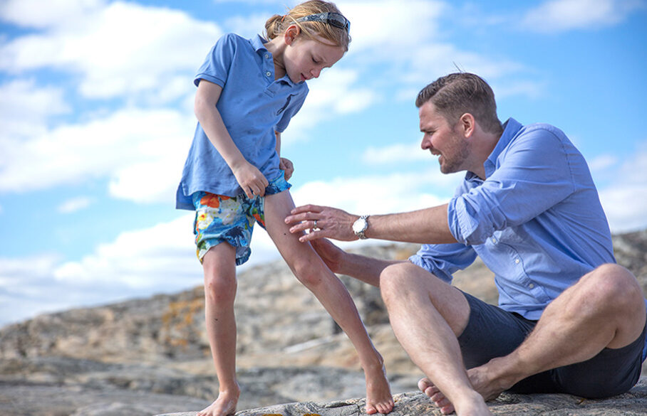 Adult assisting a child with a leg wound by outdoor rocks.