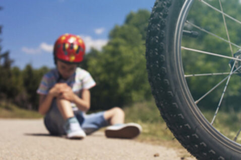 Child sitting on the ground with a scraped knee after falling off a bicycle.