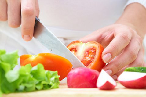 Person slicing vegetables with a knife in a kitchen.