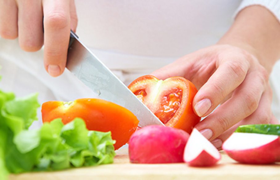 Person slicing vegetables with a knife in a kitchen.