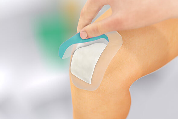 Person removing the protective strip from Sorbact Secure dressing on the knee.